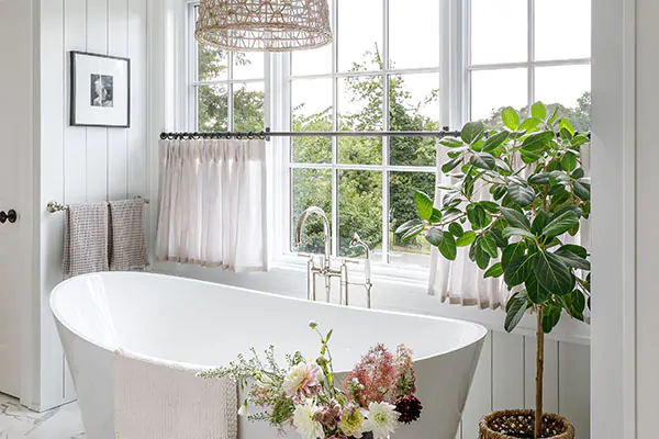A simple bathroom with an standalone tub features Tailored Pleat Cafe curtains made of Luxe Sheer Linen in Oatmeal