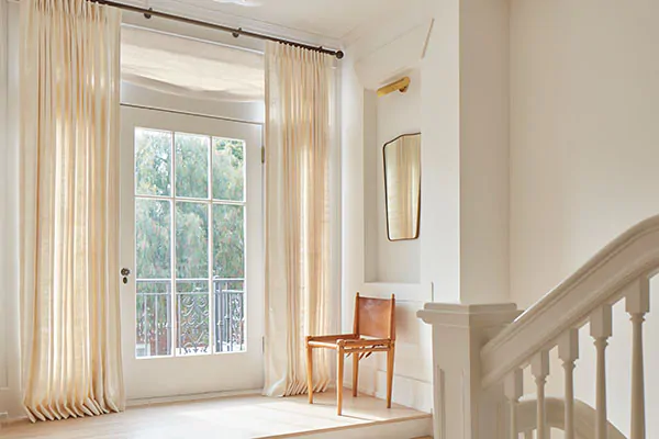 A foyer has lots of warm natural light filtered through Tailored Pleat Drapery made of Raw Silk in Glacier