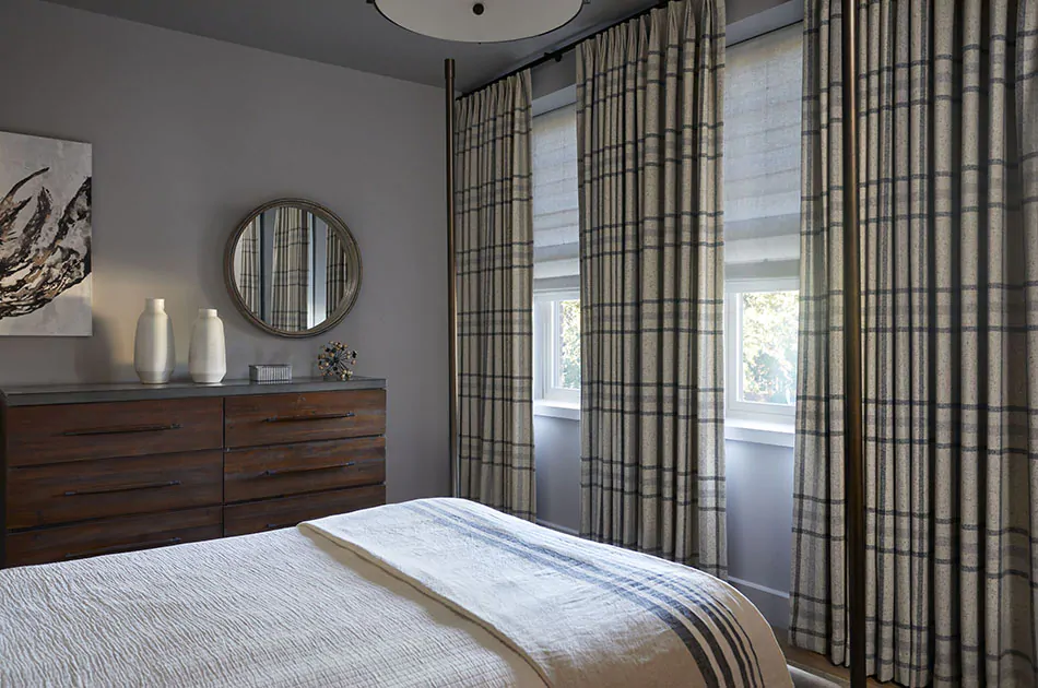 Plaid curtains adorn a cozy inn bedroom along one wall with multiple windows beside the bed and dresser