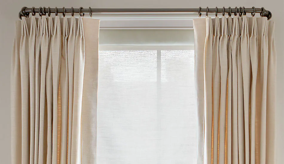 A close-up shows details of Tailored Pleat Drapery made of Alma in Beige & French return curtain rods Lafayette in Gunmetal