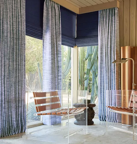 Living room curtain ideas include design drapery on a corner window paired with matching Roman Shades