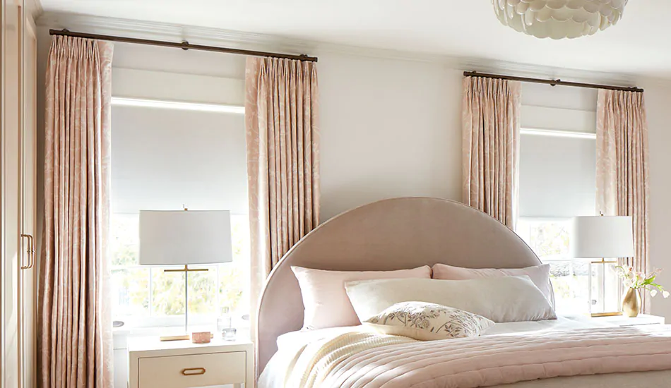 A pink and white bedroom has curtains to keep heat out made of Tailored Pleat Drapery in Chinoiserie, Blush, with lining