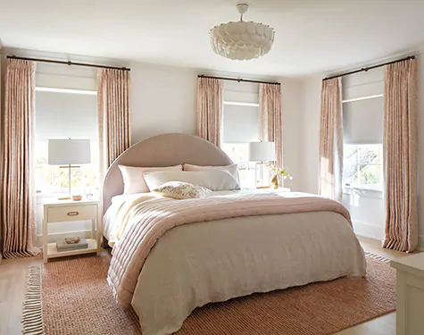 A bedroom features Tailored Pleat Drapery made of Chinoiserie in Blush with Blackout lining for a room darkening effect