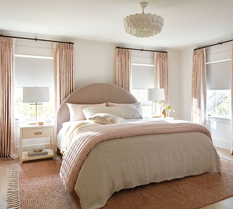 Layering styles, one of the window treatment trends 2024, is seen in this bedroom's Tailored Pleat Drapery and Roller Shades