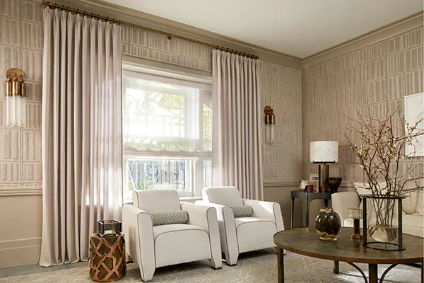 A living room has Tailored Pleat Drapery made of a sheers in a warm light brown tone to match other warm colors in the room
