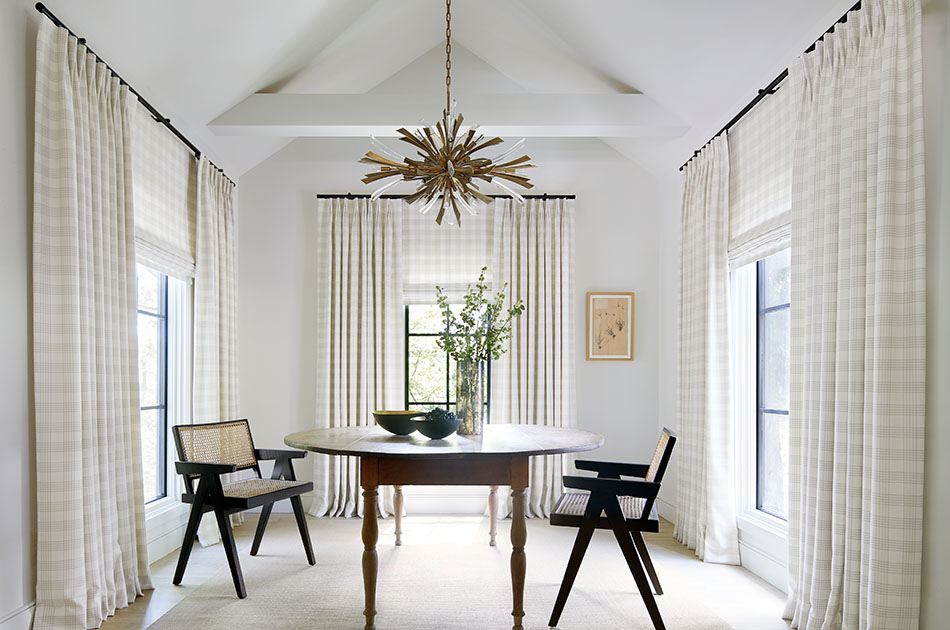 Tailored Pleat Drapery made of Emerson in Shea are paired with Flat Roman Shades of the same fabric in a bright dining room
