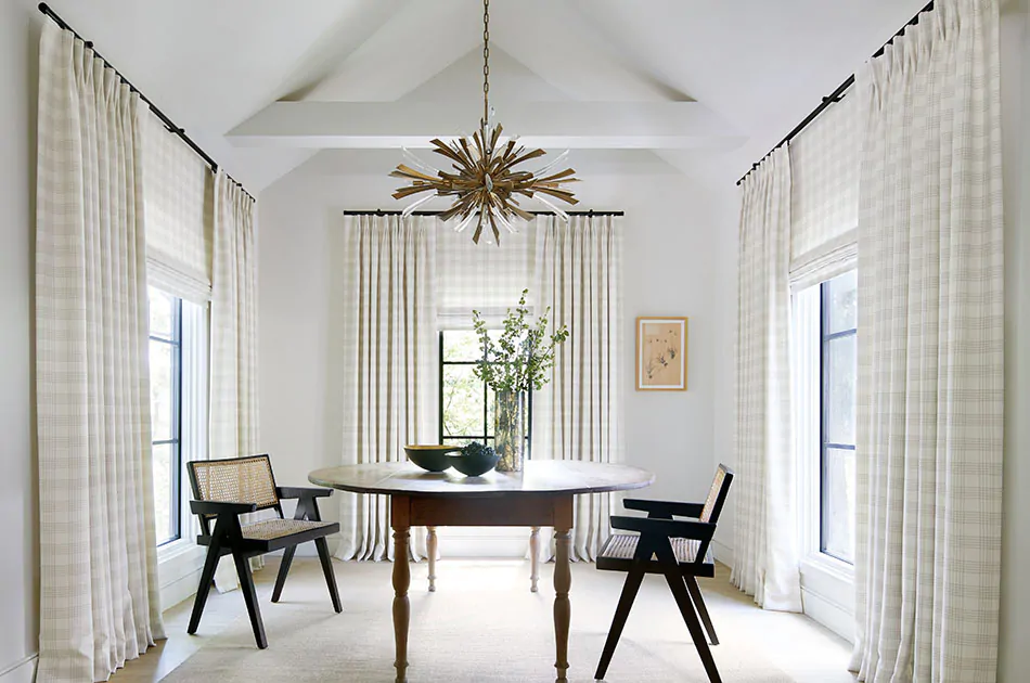 Tailored Pleat Drapery made of Emerson in Shea are paired with Flat Roman Shades of the same fabric in a bright dining room