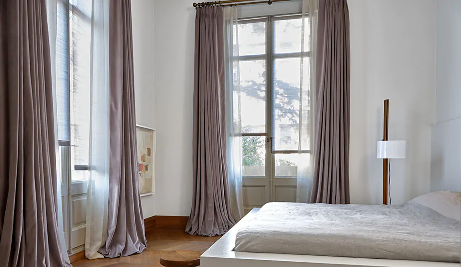A luxe bedroom has layered curtains made of Tailored Pleat Drapery in Lannister Sheer, Off-White and Posh Velvet, Heather