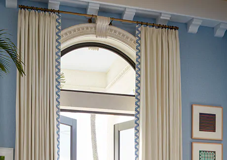 A blue room with a tall ceiling features curtains for arched windows made of Tailored Pleat Drapery in Luxe Linen, Oyster
