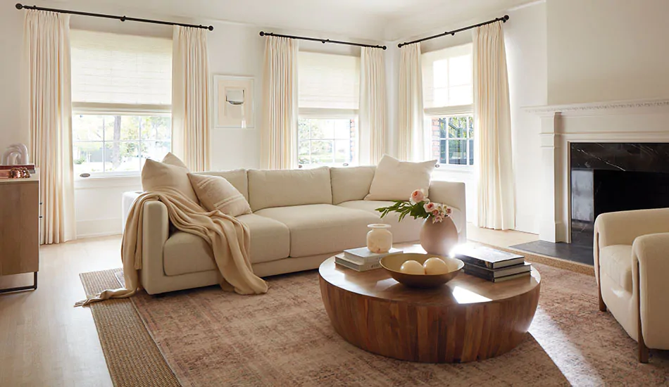 A living room with neutral tones has curtains hung high and wide showing how to hang curtains to accentuate room height