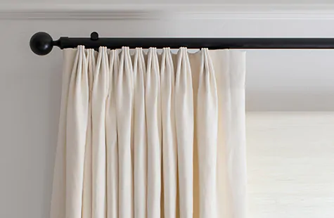 A close up of Tailored Pleat Drapery on a black track shows how to install drapes so the curtain rod extends past the window