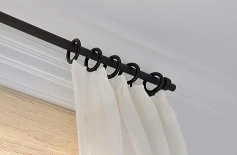 A close up of off-white sheer curtains hung on rod and ring hardware shows how to hang curtains high above the window