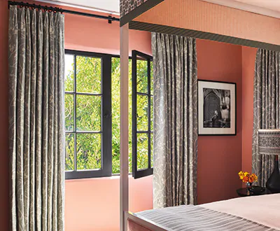 Boho curtains made of Tailored Pleat Drapery of Chinoiserie in Dove balance the bright salmon pink walls of a bedroom