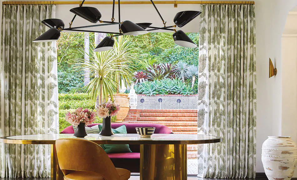 A boho-inspired dining room with jewel tones has curtain sheers made of Martyn Lawrence Bullard's Palmier in Tropical