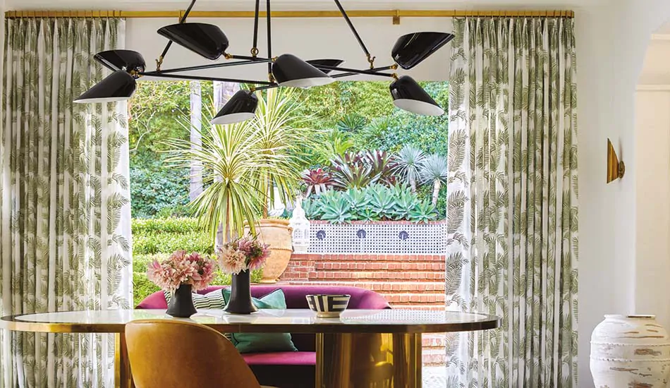 A dining room with a tropical theme shows modern curtain ideas in its Tailored Pleat Drapery made of Palmier in Tropical