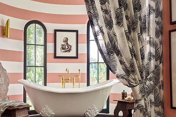 A bathroom with pink and white stripes on the walls features Tailored Pleat Drapery made of Palmier in Onyx used as a divider