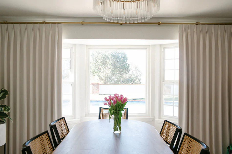 A luxurious dining room has a long dining table and Velvet Curtains in the Tailored Pleat style made of Posh Velvet in White