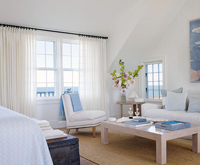 A bright coastal room features Tailored Pleat Drapery made of Sankaty Stripe in Moon to match the white walls