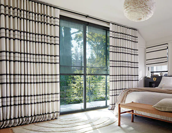 Shoreham Stripe in Jet drapery adds a bold black and white pattern to a modern bedroom, creating a striking sliding glass door curtain idea with strong visual contrast.