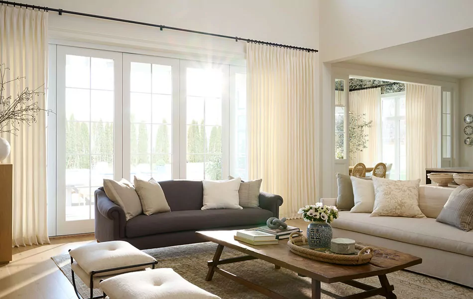 A sunny, relaxing living room with old and new styles has Tailored Pleat Drapery made of Stonewash in White