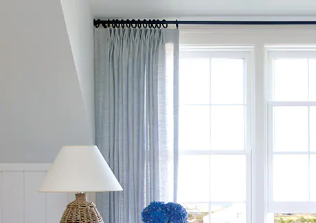 Tailored Pleat Drapery made of Breeze in Sky is mounted inside the window box with Wrought Iron hardware in Black