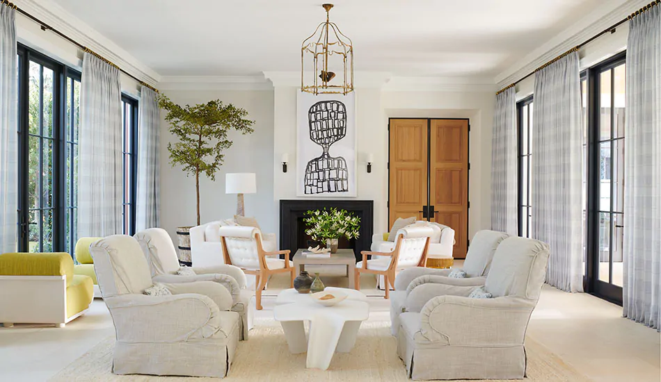 A bright open living room has white and black elements with warm wood tones and Tailored Pleat Drapery in Jasmine Sky