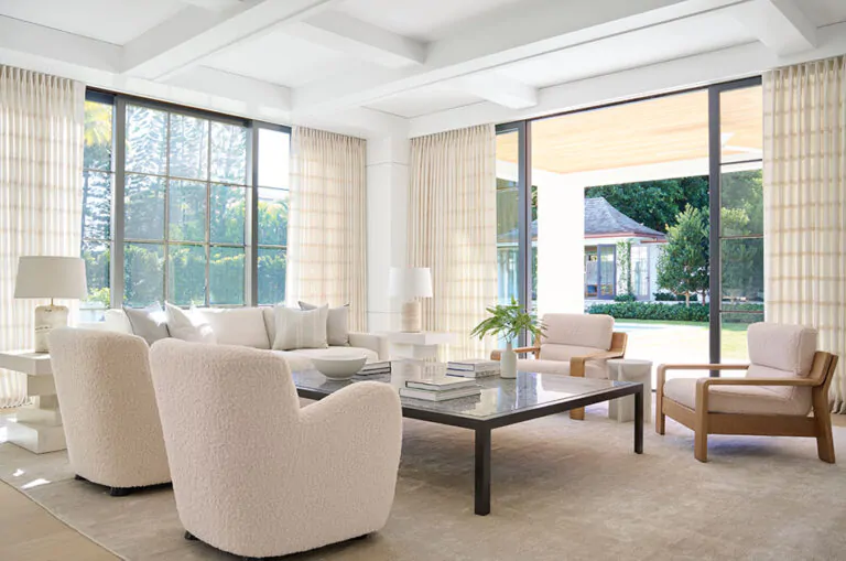 A bright, open living room features drapery panels of Tailored Pleat Drapery made of Victoria Hagan Lily in Buff hung high