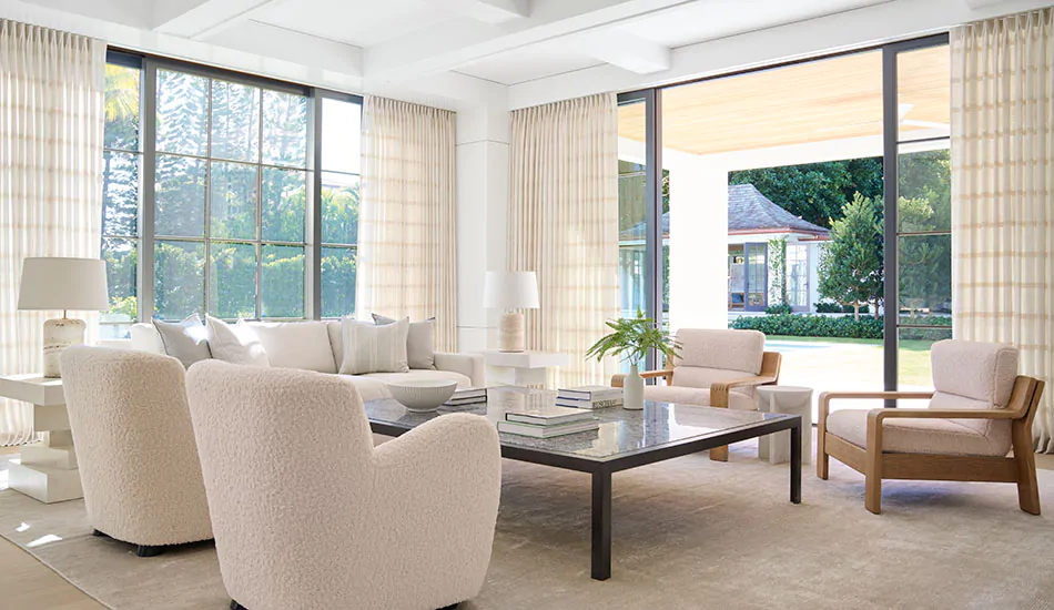 A family room with floor to ceiling windows and warm colors has Tailored Pleat Drapery made of Sankaty Stripe in Pearl