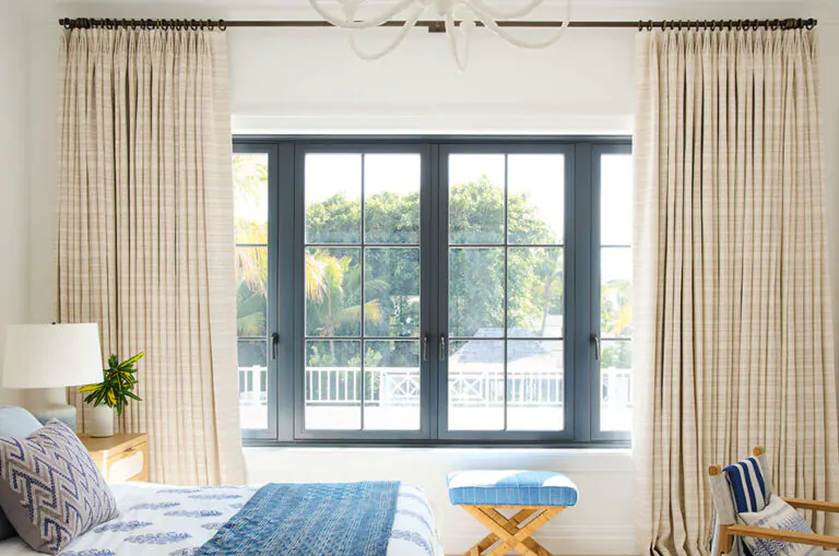 An inviting bedroom with tailored pleat drapery made of Tidal Line in Natural shows how to hang curtains to accentuate height