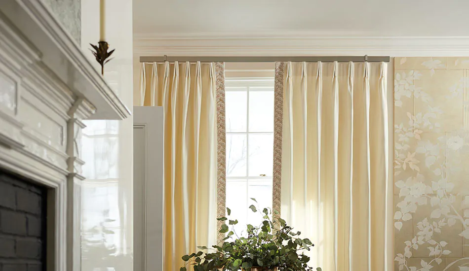 Warm-toned neutral drapery made of Wool Blend in Snow is hung high and wide above a window in a room with gilded wallpaper