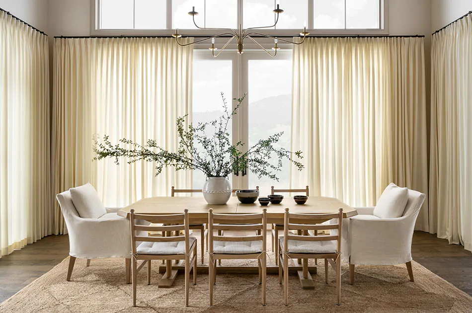 A great room with wood dining table has studio mcgee window treatments of Tailored Pleat Drapery made of Wool Blend in Snow