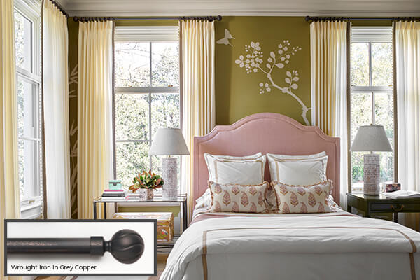 One of the window treatment trends 2024 seen in this bedroom is blending hardware in iron with ivory-colored drapery
