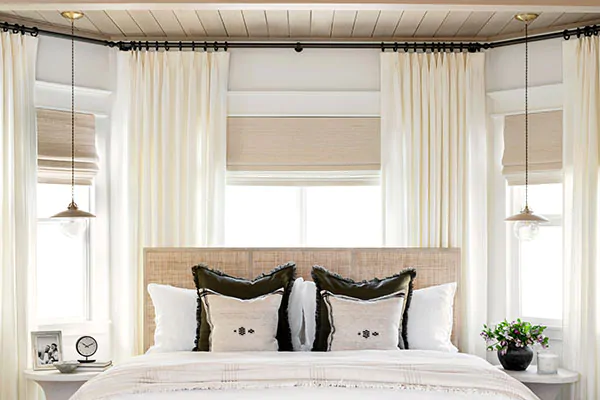 Window treatments for bay windows include Tailored Pleat Drapery layered with a Woven Shade in a modern farmhouse bedroom