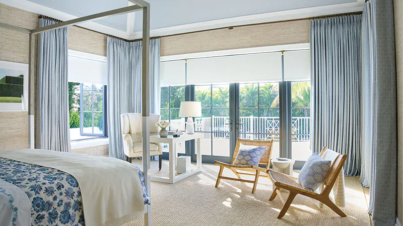 A coastal style bedroom has Tailored Pleat Drapery made of Vanda in Sky and Roller Shades made of Ava in Mist