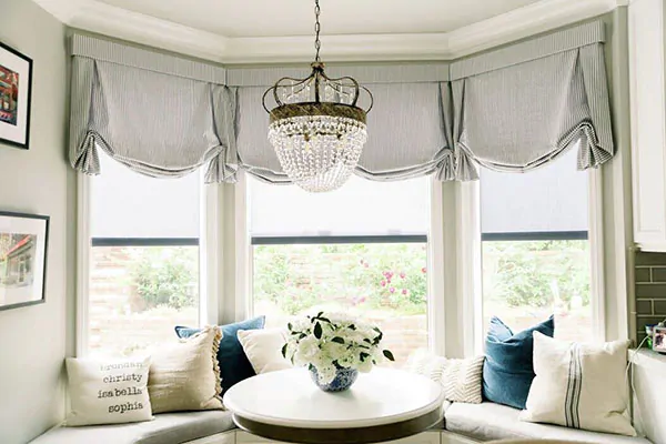 A breakfast nook features a round table and rounded window seat under Tulip Roman Shades made of Cottage Stripe in Black