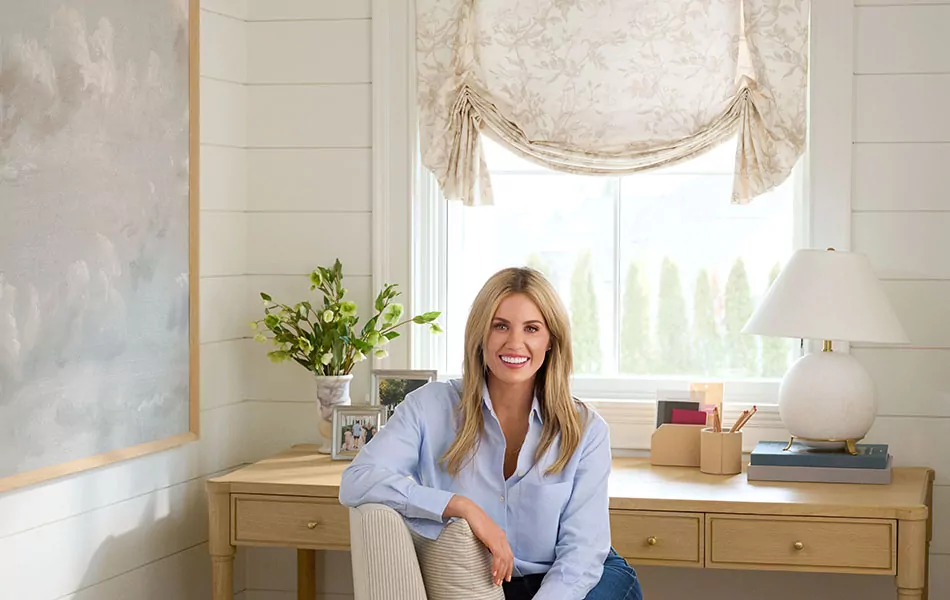 Shea McGee sits on a chair in her office which features a Tulip Roman Shade made of Wildvine in Flax