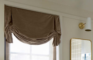 Roman shades for windows include Tulip Roman Shades made of Velvet in Camel in a living room with elegant gold-trimmed decor