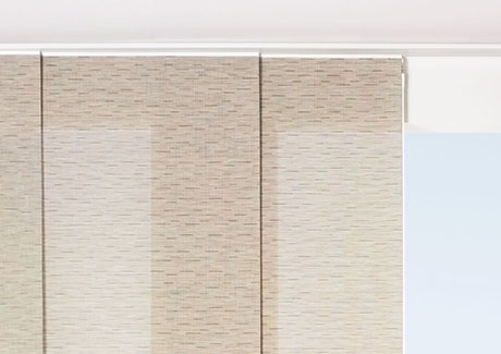 Panel track blinds made of Chilewich Bamboo in Chalk are installed in an outside mount on a white track over a tall window