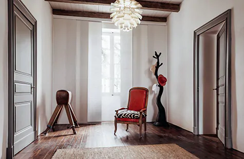 A sitting room with lots of wood tones and a few bold red accents features vertical blinds made of Ozark in Latte