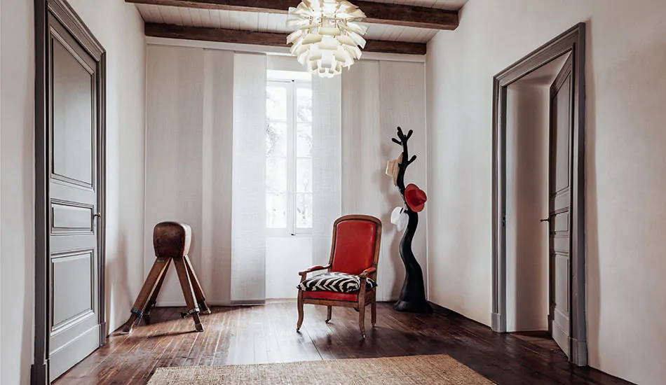 Panel track blinds made of Ozark in Latte add texture to a modern, rustic room with wood floors and a bright red chair