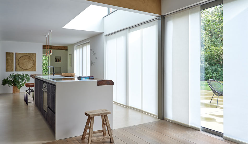 A large open kitchen features tall windows covered by vertical blinds in Park material in Winter on a panel track system