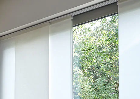 Panel track blinds made of Park in Winter are installed in an inside mount on a white track over a tall window