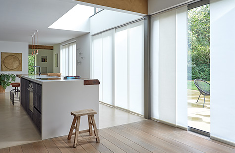 Vertical Blinds made of Park material in Winter run along a panel track in a large open kitchen with floor to ceiling windows as window coverings for large windows with privacy control