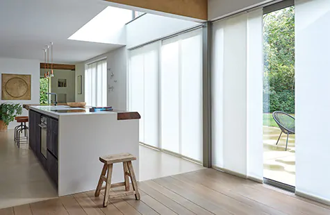 Vertical Blinds made of Park material in Winter run along a panel track in a large open kitchen with floor to ceiling windows