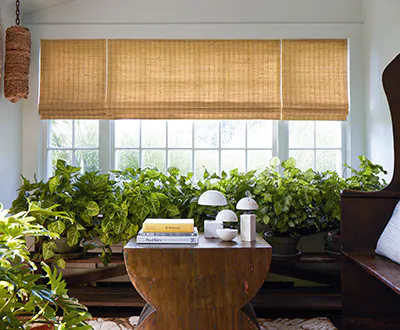 A sunroom has Woven Wood Shades made of Coastline in Oat for texture that shows the difference between blinds vs shades