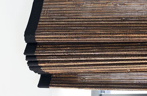 A close up of a Woven Wood Shade made of Artisan Weaves Del Rey in Shadow shows the addition of natural decorative border tape
