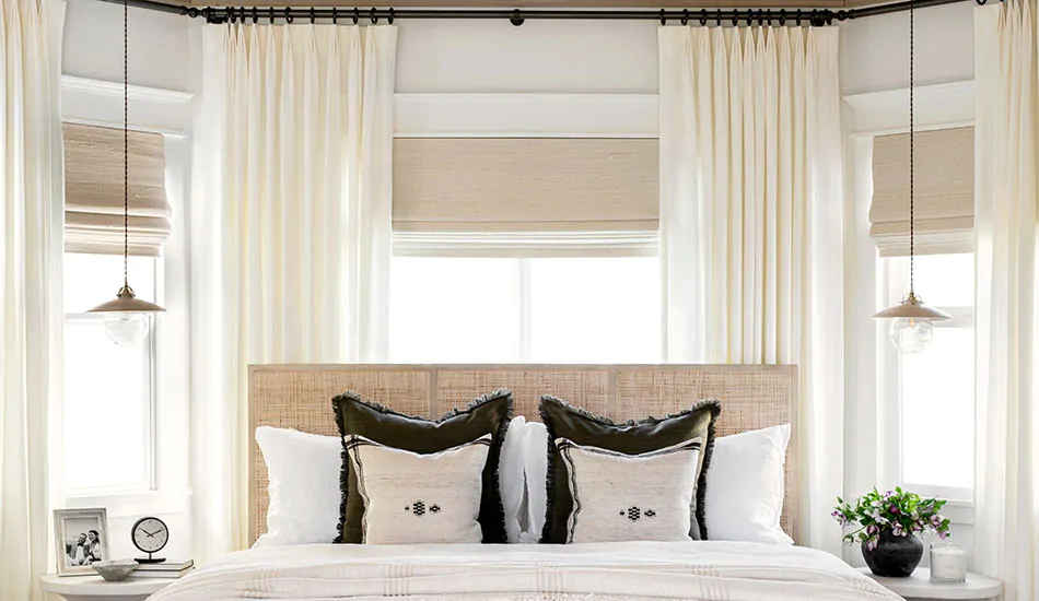 A bedroom has studio mcgee window treatments of Tailored Pleat Drapery made of Linen and Woven Wood Shades made of Bayshore