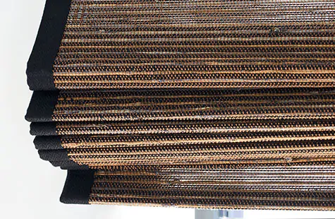 A close up of the folds of bamboo blinds made of Del Rey in Shadow show the texture of the material and border tape in black