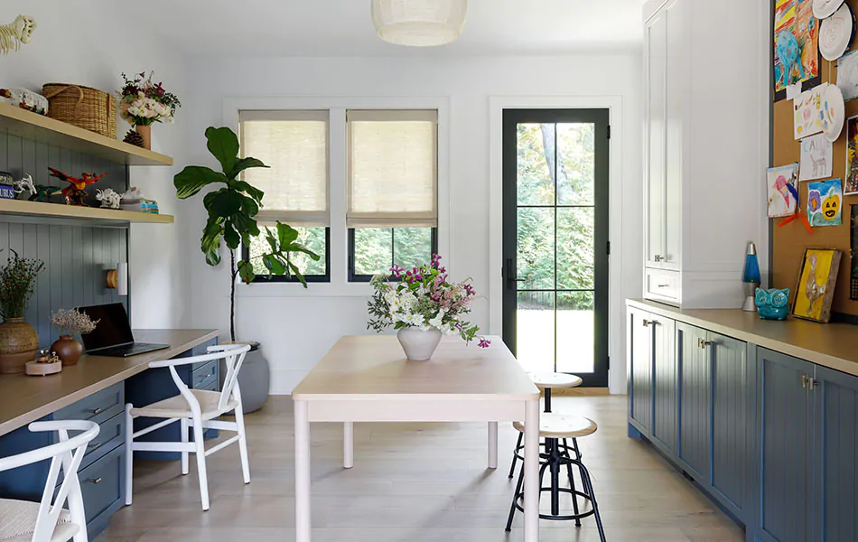 An office space with dark blue cabinets and wood tones has Waterfall Woven Wood Shades made of Grassweave in Hemp