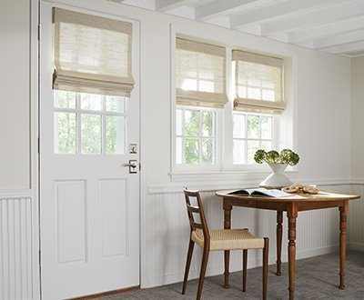 Woven shades made of Grassweave in Hemp offer an organic look to windows in a bright basement with a wood table